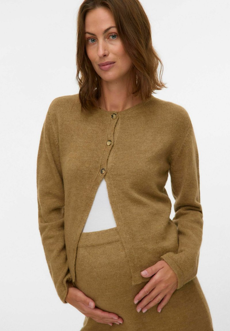 Brun strikket cardigan med rund hals, tre knapper og åpning foran. Myk tekstur, kombinert med en hvit innertrøye og matchende underdel.