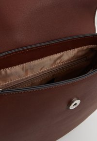 Wnętrze brązowej skórzanej torby o gładkiej fakturze, wyposażone w jasnobrązową podszewkę i kieszeń na zamek. Widoczne magnetyczne zapięcie na zatrzask.