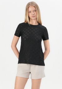 Black short-sleeve top made of laser-cut fabric with a diamond pattern. Features a round neckline and relaxed fit, paired with light beige shorts.