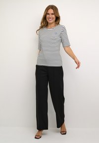 Tricou cu dungi alb-negru, cu mâneci scurte și guler rotund, combinat cu pantaloni negri cu croială lejeră și sandale minimaliste negre.