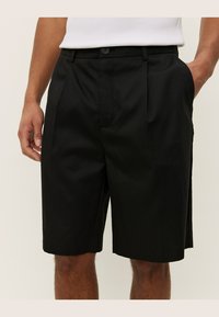Pantaloni shorts neri su misura con una texture liscia, pence frontali, tasche laterali e chiusura a bottone in vita.