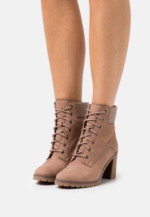 Stivaletti in suede marrone con design allacciato, punta arrotondata e tacco spesso. Presentano una caviglia imbottita e eyelets metallici per i lacci.