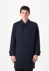 Mørkeblå trenchcoat med krage, knappelukking og lange ermer. Har rette linjer og en jevn tekstur.