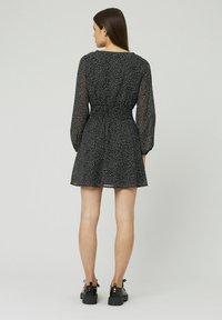 Robe noire à pois blancs, avec de longues manches transparentes et une taille cintrée. Jupe évasée avec une texture lisse, associée à des chaussures noires.