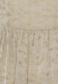 Tela de un beige claro con un sutil patrón abstracto. Presenta una textura recogida en la parte inferior. Material suave y ligero.