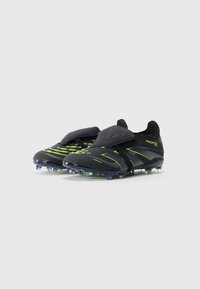 Black and neon green soccer cleats with text "Predator" on side, studded sole, and a Velcro strap over the laces on a white background.