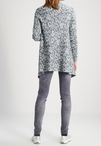 Světle modrý svetr s dlouhým rukávem a šedým leopardím potiskem, s delším zadním lemem. V kombinaci se šedými skinny džíny a bílými teniskami.