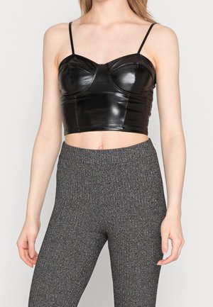 Femme portant un crop top ajusté en similicuir noir à fines bretelles et un pantalon taille haute en maille texturée grise.