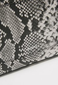 Gros plan d'une surface à motif peau de serpent noir et blanc avec des coutures visibles et le nom de la marque ALDO en texte blanc.