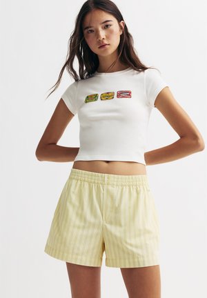 Vit kortärmad t-shirt med färgglada matgrafik; matchad med gula randiga shorts med elastisk midja och knappdetalj.