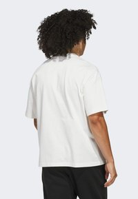 Biały bawełniany t-shirt z krótkim rękawem, luźny krój i okrągły dekolt. Widok z tyłu pokazuje gładką fakturę i minimalne detale projektowe.