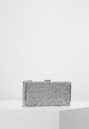 Lille rektangulær sølvglitrende aftenkobling med metallisk ramme og kæderem, vist på hvid piedestal mod ensfarvet baggrund.