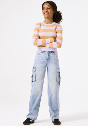 Pull rayé orange et lavande, jeans cargo taille haute bleu clair avec poches sur le côté, chaussures noires avec des rayures blanches.