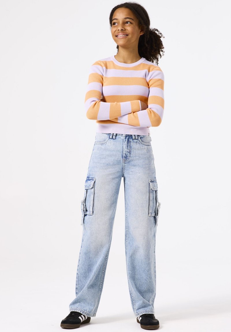 Gestreepte trui in oranje en lavendel, hoogopgemakte lichtblauwe cargospijkerbroek met zijzakken, zwarte schoenen met witte strepen.