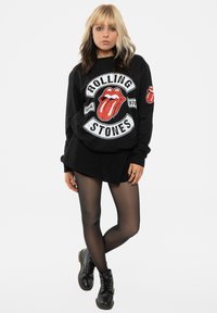 Black sweatshirt featuring Rolling Stones logo with red lips, paired with a black mini skirt, sheer black tights, and black lace-up boots.