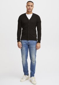Svart cardigan med ribbete skuldre, seks knapper, tykk strikket stoff, kombinert med lyseblå smal jeans og hvite sneakers. Enkelt, uformelt antrekk.