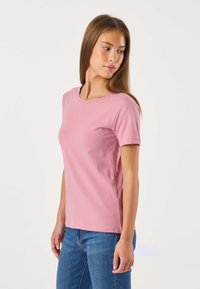 T-shirt rosa di cotone con maniche corte, scollo rotondo e silhouette aderente, abbinata a jeans blu. Tessuto liscio, senza motivi o dettagli.