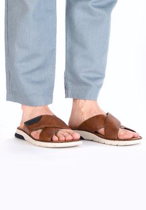 Braune Ledersandalen mit gekreuzten Riemen und einem strukturierten Stoffakzent, ausgestattet mit einer weißen Sohle und einer schwarzen Untersohle.