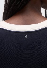 Laivastonsininen teksturoitu villapaita, jossa on kermaisen värinen ribbineuloskaulus ja pieni pyöreä hopeinen merkki, jossa on 'BOBE'-logo niskan takana.