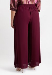 Pantaloni larghi bordeaux con una texture morbida e fluida, dotati di una vita elastica e una silhouette fluida, impreziositi da pannelli trasparenti.