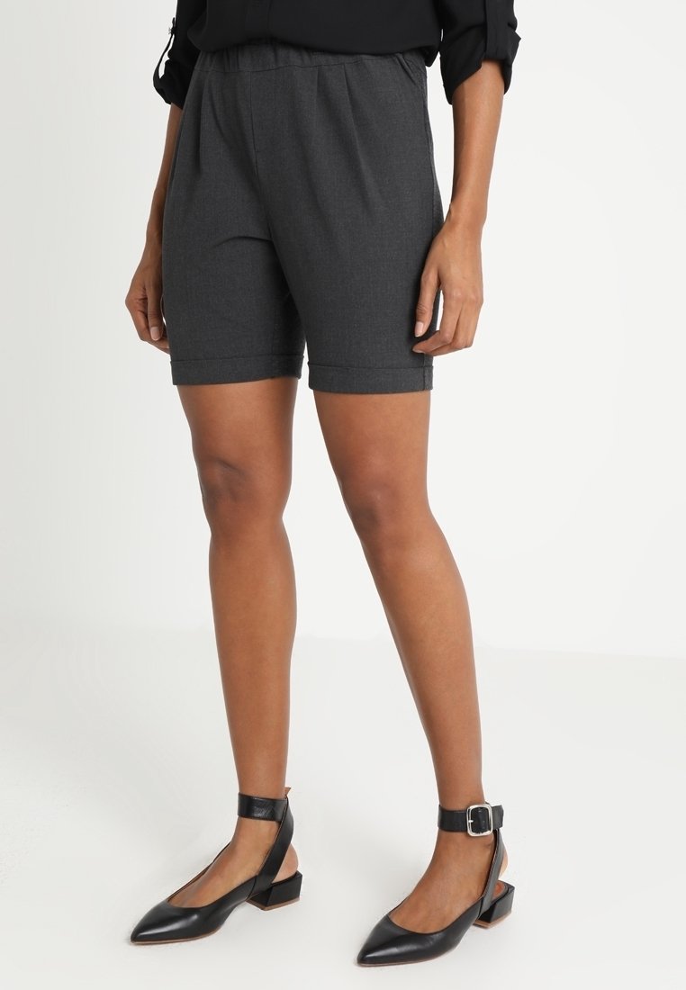 Shorts gris ajustés avec une taille élastique, atteignant le milieu de la cuisse. Associés à des chaussures noires à bride de cheville et à talons carrés.