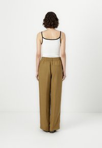 Top blanco sin mangas con tirantes negros, combinado con pantalones holgados de talle alto en una tela marrón clara. Detalle visible del bolsillo trasero.