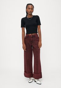 Top corto a righe nere, abbinato a pantaloni in denim bordeaux larghi con risvolto, indossato con sandali bianchi.
