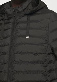 Chaqueta acolchada negra con cremallera frontal, capucha y cordones elásticos. Presenta un patrón acolchado vertical y detalles en metal plateado.