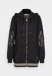 Černá mikina s kapucí s krajkovými doplňky na rukávech, stříbrným zipem a šňůrkami. Má dvě přední kapsy a proužkovaný žebrovaný lem.