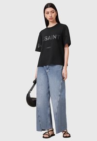 Sort T-shirt med korte ærmer og prægede bogstaver, parret med lyse denim bukser med bred ben. Sandalerne har tynde stropper og en flad sål.