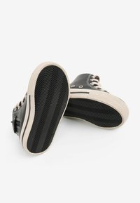 Sorte kanvas højhælede sneakers med beigefarvede gummisåler, der har flade snørebånd og metaløjer, og viser et struktureret herringbone mønster på sålen.