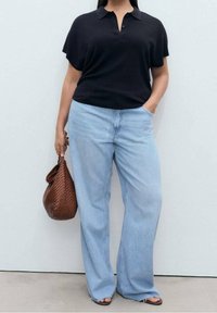 Czarna koszulka polo z kołnierzykiem, zestawiona z jasnoniebieskimi szerokimi dżinsami. Stylizację dopełnia brązowa pleciona torebka i sandały na odkryte palce.