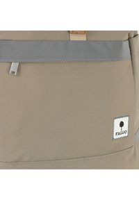 Sac à dos en tissu beige avec des accents gris, doté d'un patch logo brodé et de détails en métal sur la poche avant.