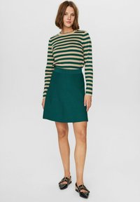 Grön A-linjeformad kjol med en texturerad yta. Kombinerad med en randig långärmad topp i grönt och beige. Svarta slip-on skor med nitar.