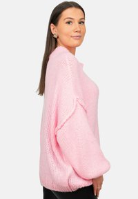 Overmaatse roze gebreide trui met losse mouwen, geribbelde zoom en een textuurstof. Gecombineerd met zwarte leggings. Ronde halslijn.