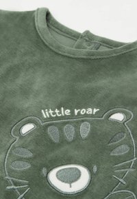 Grünes Fleece-Shirt mit einem Bärenkopf-Design, das mit Stickdetails versehen ist, und dem Text "little roar" darüber. Rundhals mit Druckknopfverschluss.