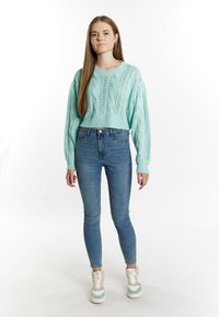 Maglione corto lavorato a maglia blu chiaro con motivi a treccia, abbinato a jeans aderenti e sneakers chunky multicolori.