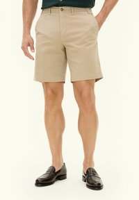 Pantaloni chino khaki con taglio dritto, tasche laterali e una texture liscia. Abbinati a mocassini in pelle scura per un look elegante.