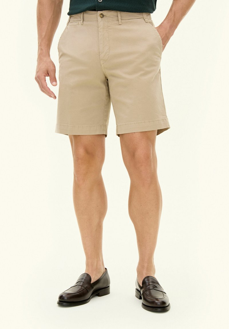 Pantaloni chino khaki con taglio dritto, tasche laterali e una texture liscia. Abbinati a mocassini in pelle scura per un look elegante.