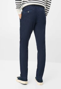 Pantaloni in denim blu navy con gambe dritte, caratterizzati da due tasche posteriori con chiusura a bottone e una texture sottile. Indossati con scarpe casual.