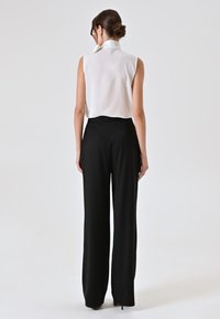 Witte mouwloze blouse met kraag, gecombineerd met high-waisted zwarte broek; gladde stof, grote pijpen en een getailleerde pasvorm.