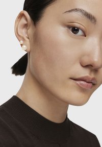 Złote kolczyki z perłami o unikalnym designie, z dwiema białymi perłami różnej wielkości i zakrzywionym złotym akcentem.