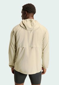 Hell-beige Kapuzenjacke mit lockerer Passform, ausgestattet mit einem Rückentlüftungspanel, langen Ärmeln und glattem, wasserabweisendem Material.
