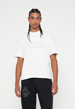 Balts īsām piedurknēm T-krekls ar grafisku tekstu gaiši pelēkā krāsā, savienots ar melniem sporta biksēm, kuru sānos ir pelēkas liesmas logotips.