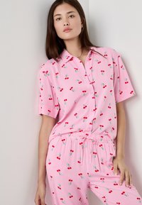 Pigiama rosa a maniche corte con righe bianche e un motivo di ciliegie. La parte superiore ha un colletto e bottoni, con pantaloni a vita elastica.