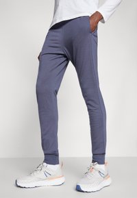 Dark blue jogger pants, slim fit, soft fabric, with side pockets and ankle cuffs, paired with light gray athletic shoes.