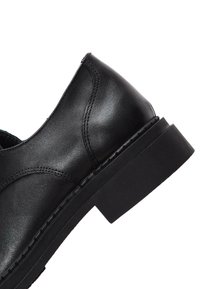 Chaussure habillée en cuir noir avec un talon bloc bas et des coutures visibles le long du côté et du panneau arrière.
