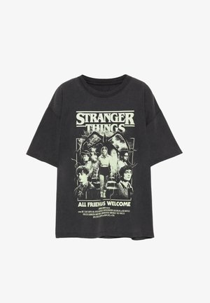 Sötétszürke, túlméretezett póló, amelyen a "Stranger Things" karaktereinek grafikája és a "All Friends Welcome" felirat világoszöld színben szerepel.