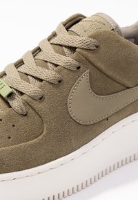 Zapatillas de ante verde oliva con parte superior texturizada, puntera redonda, cordones a juego y suela de goma blanca. Presenta un acento de logo bordado.