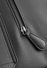 Black textured leather featuring a silver zipper and a leather zipper pull. Notable stitching adds detail along the edges.